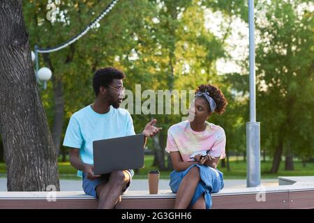 Afrikanisches junges Paar, das am Laptop arbeitet und online diskutiert, arbeitet zusammen, während es draußen sitzt Stockfoto