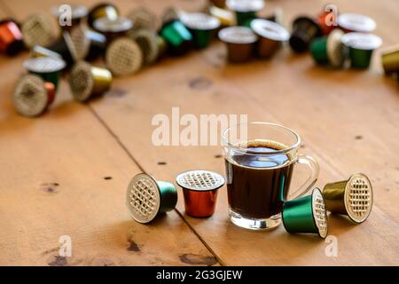 Kaffeebecher aus klarem Glas, umgeben von gebrauchten Kaffeepads auf einem Holztisch. Stockfoto