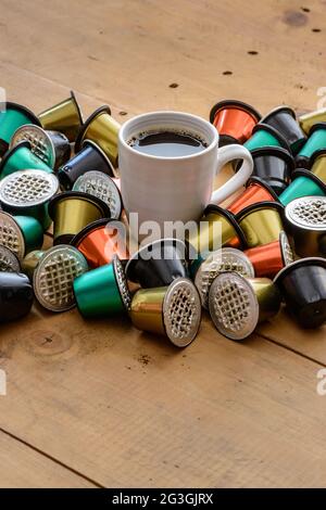 Kaffeetasse umgeben von gebrauchten Kaffeekapseln auf Holztisch. Stockfoto
