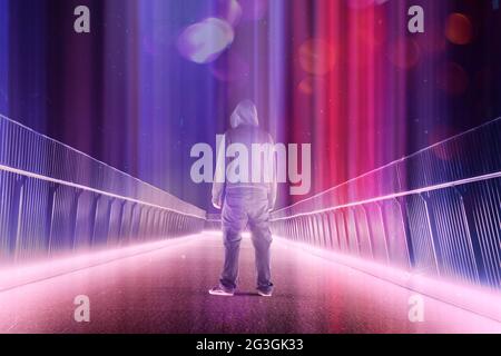 Eine geheimnisvolle Kapuzenfigur, die nachts mitten auf einem Pfad steht. Silhouetten gegen helle Lichter. Überlagert mit einer Neon-, Retro-, Dampfwelle Stockfoto