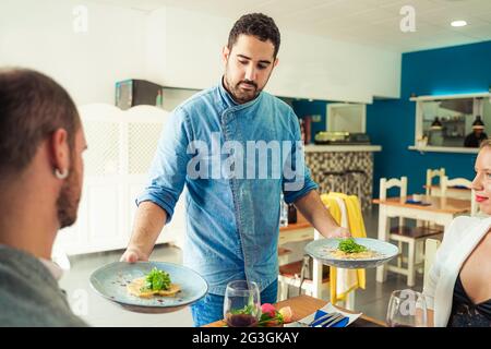 Kellner, der zwei Teller mit Pastaravioli für ein jüngeres Paar im Restaurant trug. Food and Job-Konzept. Stockfoto