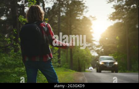 Mann mit Rucksack, der ein Auto auf der Straße fängt. Fahren Sie mit dem Auto-Stop. Stockfoto