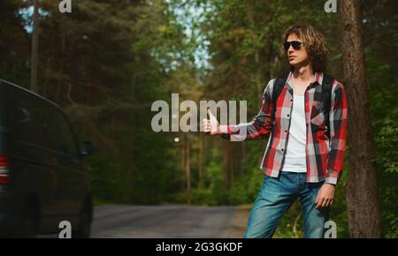 Mann mit Rucksack, der ein Auto auf der Straße fängt. Fahren Sie mit dem Auto-Stop. Stockfoto