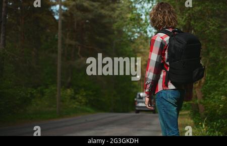 Mann mit Rucksack, der ein Auto auf der Straße fängt. Fahren Sie mit dem Auto-Stop. Stockfoto