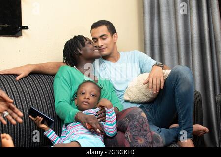 Interracial paar mit einer guten Zeit zusammen sitzen auf der Couch. Kleine Tochter hält ein Telefon Stockfoto