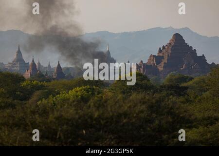 Rauch von einem Feuer bei Sonnenuntergang zwischen den alten buddhistischen Tempeln in der Stadt Bagan, Myanmar, einschließlich des berühmten Dhammayangyi-Tempels Stockfoto