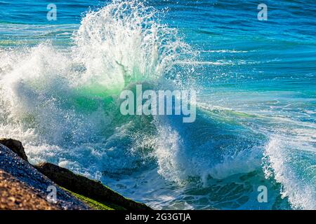 Wellen brechen in der Sommermorgendsonne gegen die Felsen am Strand Stockfoto