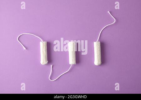 Drei weiche, schützende und saugfähige Tampons aus Baumwolle für die Damenpflege auf fliedernem Hintergrund. Draufsicht. Horizontale Zusammensetzung. Stockfoto