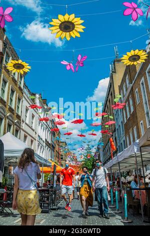 London, Großbritannien. Juni 2021. Ein walisischer Fan kommt am Tag des nächsten Spiels in Wales bei den Euros an einem heißen und sonnigen Tag in Chinatown vorbei - Shaftesbury enthüllt eine immersive Installation des Botanischen Gartens über der Londoner Gerrard Street in Chinatown. Es werden sieben verschiedene Blumenarten gezeigt, darunter Sonnenblumen, chinesische Pfingstrosen, Pfirsichblüte und Orchideen. Kredit: Guy Bell/Alamy Live Nachrichten Stockfoto