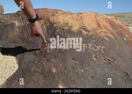 Die Hand des Menschen führt auf uralte Felsschnitzereien einer wahrscheinlich nicht identifizierten frühen Form arabischer Briefe, die vor 2000 Jahren von Nabateans Kamelreitern geschrieben wurden Stockfoto