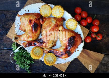 Gegrillte Hühnerschenkel mit Gemüse, Souce, Mais, Kirschtomaten, Kräutern. Lebensmittelhintergrund. Draufsicht Stockfoto