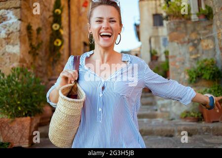 Reisen Sie in Italien. Glückliche stilvolle Frau mittleren Alters mit Strohsack Sightseeing in Pienza in der Toskana, Italien. Stockfoto