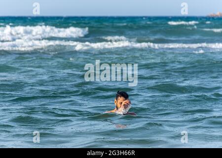 Ein junger Mann ertrinkt im Meer und winkt mit der Hand um Hilfe. Stockfoto