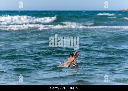 Ein junger Mann ertrinkt im Meer und winkt mit der Hand um Hilfe. Stockfoto