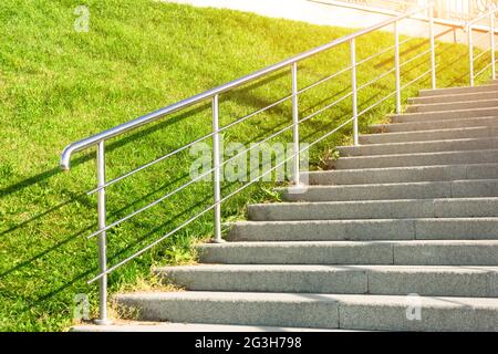 Steintreppe, die den Hang mit Rasengras, glänzendem Metall und Geländer hinauf führt Stockfoto