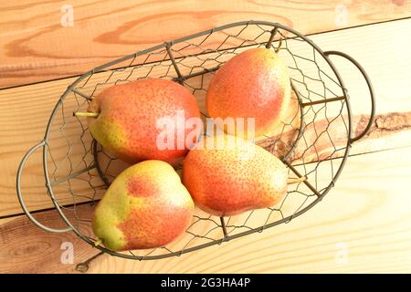 Mehrere reife gelb-rote Birnen in einem Korb, auf einem Holztisch, Draufsicht. Stockfoto