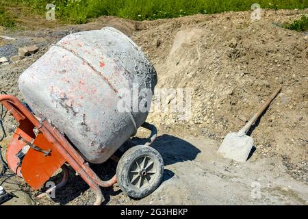 Fahrbarer Betonmischer auf dem Hintergrund eines Pfahls aus Kies. Vorbereitungsarbeiten für die Vorbereitung der Betonmasse. Nahaufnahme. Selektiver Fokus. Stockfoto