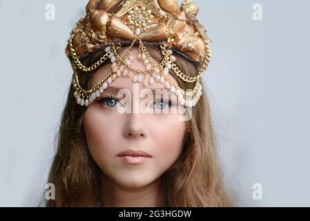 Crop Porträt der Fantasie Frau echte Meerjungfrau mit Dreizack Mythos Göttin des Meeres mit goldenen Schwanz. Gold Haar Krone Muscheln Perlen Schmuck. Meerjungfrau sitzt Stockfoto