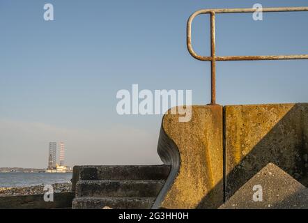 Die Strandpromenade bei Grain mit Blick auf den Hafen von Sheerness, mit Ölplattform in der Swale vertäut Stockfoto