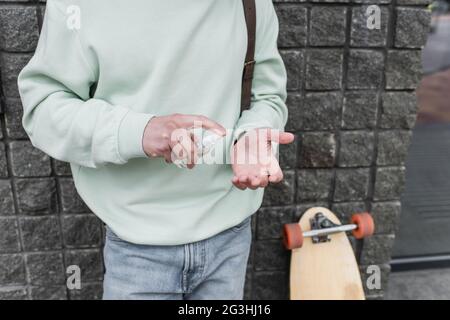 Beschnittene Ansicht des Mannes, der Desinfektionsmittel auf die Hand in der Nähe von verschwommenem Longboard anwendet Stockfoto