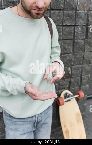 Beschnittene Ansicht eines bärtigen Mannes, der Desinfektionsmittel auf die Hand trägt Stockfoto