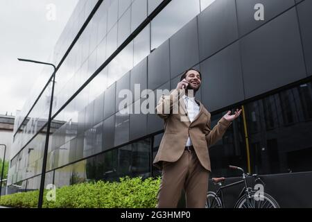 Blick aus der Nähe des Gebäudes auf einen glücklichen Geschäftsmann, der mit dem Handy telefoniert Stockfoto