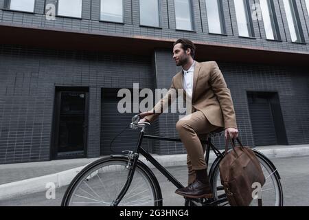 Junger Geschäftsmann in formeller Kleidung mit brauner Ledertasche und Fahrrad im Freien Stockfoto