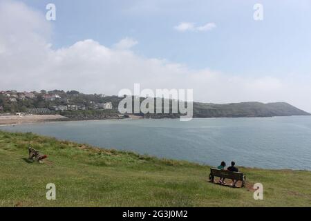 Ein Foto eines Paares saß auf einer Bank an einem Aussichtspunkt mit Blick auf das Meer in der Langland Bay, Gower Peninsula, Wales Stockfoto