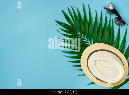 Hut, Sonnenbrille und Palmblatt auf sommerblauem Hintergrund. Overhead, Reisekonzept. Stockfoto