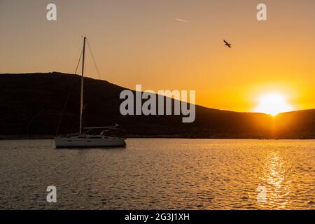 Magischer, lebhafter orangefarbener Sonnenuntergang über dem Hügel und dem Mittelmeer mit einer Silhouette eines Segelbootes, während der Vögel fliegen, in einer Bucht auf der Insel Rineja Stockfoto