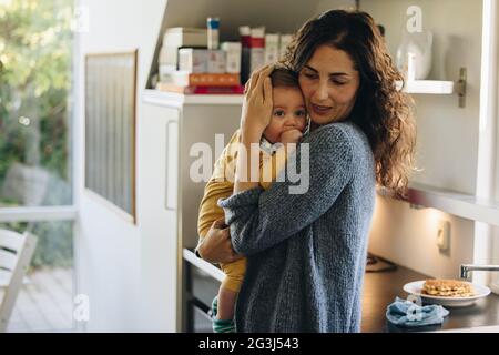 Mutter tröstet ihr Baby. Frau hält ihr Baby, während sie in der Küche steht. Stockfoto