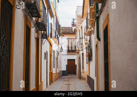 Die Außenfassaden des Gebäudes sind weiß und gelb gestrichen und eine leere schmale Straße in Córdoba, Spanien Stockfoto