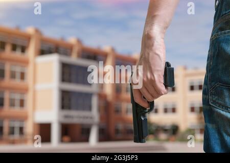 Ein junger bewaffneter Mann hält an einem öffentlichen Platz in der Nähe der High School eine Pistole in der Hand. Konzept der Pistolensteuerung. Stockfoto