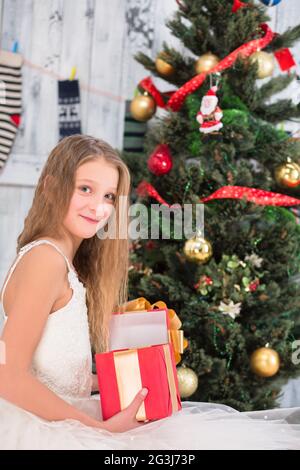 Teenager-Mädchen öffnet eine Box mit Weihnachtsgeschenk in der Nähe von Neujahrsbaum Stockfoto