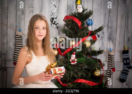 Teenager-Mädchen hält Weihnachtsgeschenk vor dem Neujahrsbaum Stockfoto