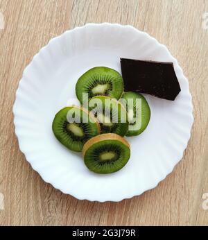 Ein paar Kiwi-Stücke und ein Stück dunkle Schokolade auf einem weißen Teller Stockfoto