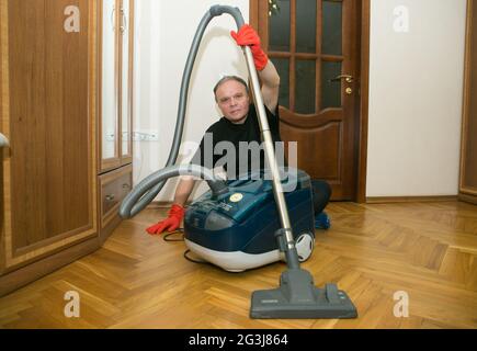 Emotionen eines Mannes mittleren Alters vor der Reinigung einer Wohnung. Tägliche Reinigung der Räumlichkeiten. Humor.EIN Mann hält einen Staubsauger in den Händen. Stockfoto