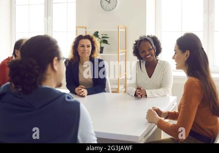 Gruppe von glücklichen, interessierten Mitarbeitern, die in einem Unternehmensmeeting am Bürotisch sitzen Stockfoto