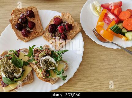 Vier gesunde Sandwiches mit dunklem Vollkornbrot. Zwei herzhafte und zwei süße Sandwiches. Eine Portion frisches Gemüse Stockfoto