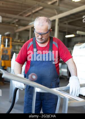 Arbeiter mit blauem Kragen, der ein Metallstück in einer Produktionsstätte poliert. Polierer beschäftigt und konzentriert während der Arbeit in einer Fabrik. Stockfoto