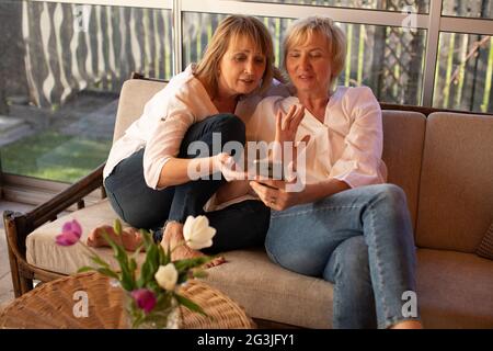 Zwei 55-jährige Frauen nutzen Smartphones, um soziale Netzwerke und Lifestyle-Fotos zu lesen Stockfoto