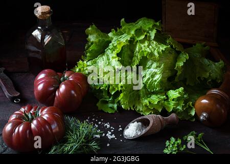 Frischer Bio-Salat, Tomaten, eine Flasche mit Kürbiskernöl auf einem alten Holztisch, das Konzept von gesunder Ernährung und Vegetarismus, Low-Key-Stil Stockfoto