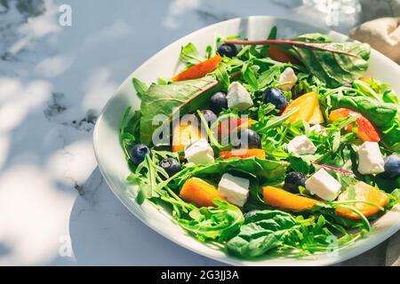 Frischer, hausgemachter Salat mit Nektarinen, Heidelbeeren, Rucola, Spinat und Feta-Käse auf weißem Marmorboden mit Schatten. Sommer-Mittagessen im Garten. H Stockfoto