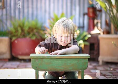 Happy adorable blonde australische Kind sitzt und lehnte sich auf einem kleinen Schultisch in der Heimat Hof Stockfoto