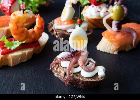 Eine Auswahl an traditionellen spanischen Speisen und italienischen Sandwiches - Tapas und Bruschetta auf einem Servierbrett. Das kreative Sandwich im Vordergrund besteht aus Stockfoto