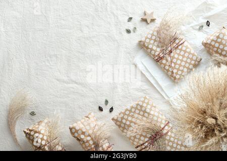 Handgemachte Geschenke in beigefarbenem Bastelpapier mit trockenem Wildgras gewickelt, das mit Baumwollschnur gebunden ist. Geometrisch flach Lay-on-weißen Textil mit natürlichen Stockfoto