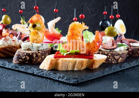 Spanische Tapas – Hier werden traditionelle spanische Sandwiches mit Meeresfrüchten serviert. Im Vordergrund Tapas mit gebratenen Garnelen, rotem Pfeffer und grünem Lettu Stockfoto
