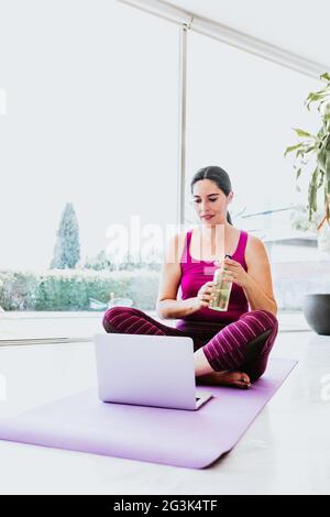 hispanische Frau, die zu Hause in Lateinamerika auf dem Boden sitzt und sich Yoga-Videos auf dem Laptop ansieht Stockfoto