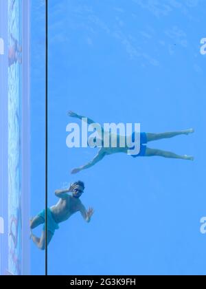 London, Großbritannien. Zwei Schwimmer schauen durch die Basis des Transparent Sky Pools in Embassy Gardens und winken Menschen an, die 115 Fuß/200 m weiter unten vorbeikommen. Stockfoto