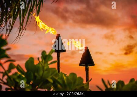 Hawaii Luau Party Maui Feuer Tiki Fackeln mit offenen Flammen brennen bei Sonnenuntergang Himmel Wolken in der Nacht. Hawaiian kulturelle Reise Urlaub Hintergrund. Stockfoto